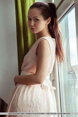 Girl in a summer dress has a big leather armchair where she rests in the nude
