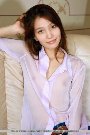 Oriental teen in jeans comfortably sat on the sofa in the run-up to striptease