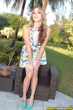 Slim blonde with long hair shows assets while sitting alone in backyard