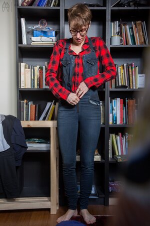 Naked short-haired girl with glasses puts clothes on right in the library