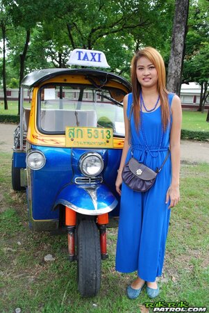 Hot female from Thailand poses in her slinky blue dress by a small taxi