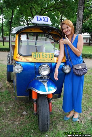 Hot female from Thailand poses in her slinky blue dress by a small taxi