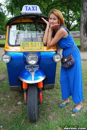 Hot female from Thailand poses in her slinky blue dress by a small taxi