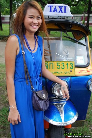 Hot female from Thailand poses in her slinky blue dress by a small taxi