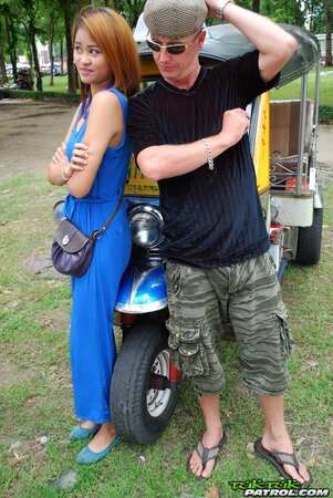 Hot female from Thailand poses in her slinky blue dress by a small taxi