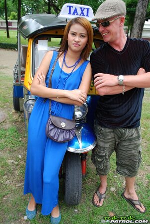 Hot female from Thailand poses in her slinky blue dress by a small taxi