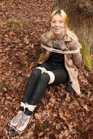 Girl with glasses can't stand up because she is hogtied by the tree