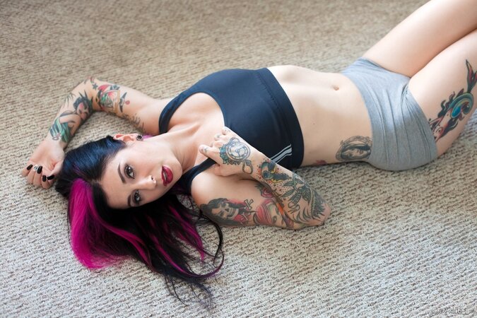 Tattooed woman poses in bedroom in lingerie that accentuates her assets