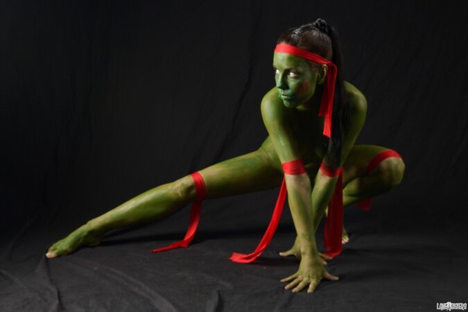Girl in the image of a naked warrior covered in green paint in combat poses