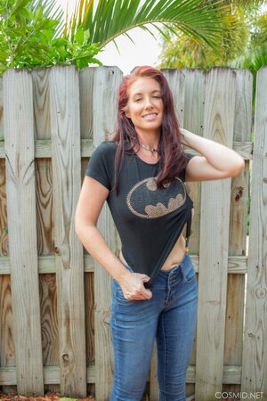 Sexy red-haired MILF takes off everything and poses all naked by the fence