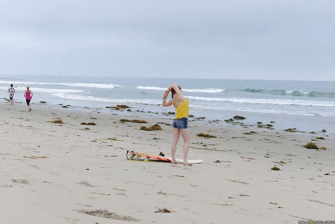 Redhead colleen in swimsuit is playfully posing with surfboard on the beach