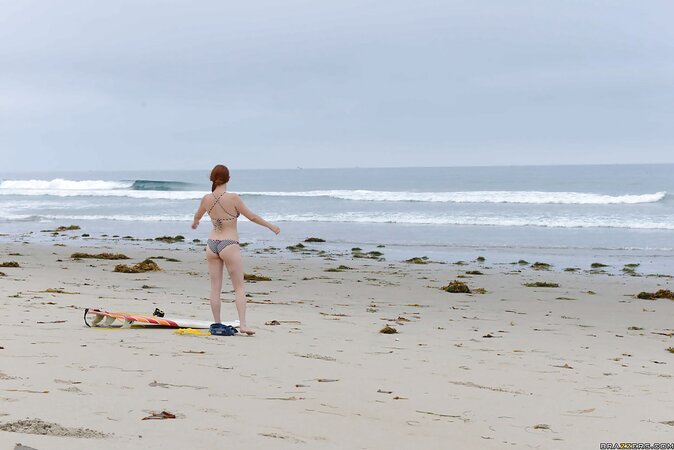 Redhead colleen in swimsuit is playfully posing with surfboard on the beach